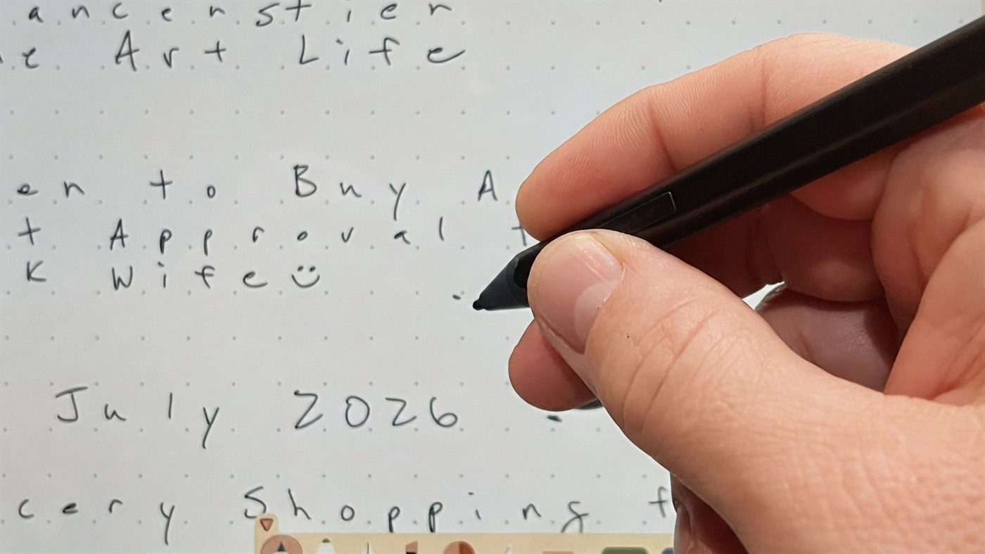 A hand holding a stylus over a Mementa dot grid page, with the flat barrel button visible on the side of the pen